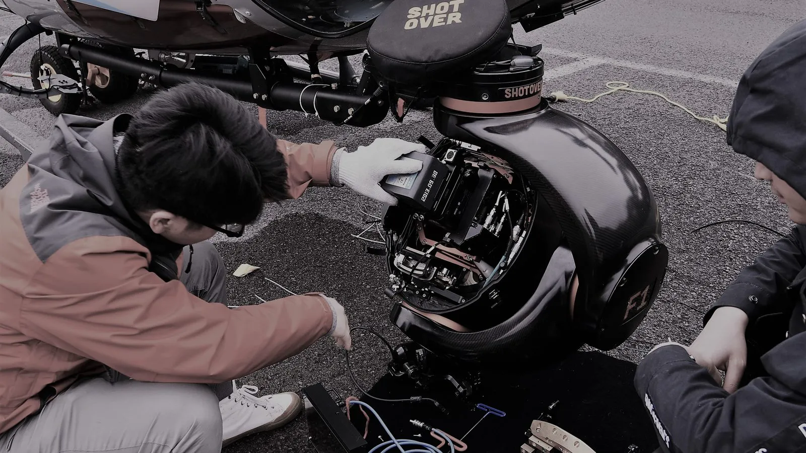 Technicians preparing a Shotover gimbal camera mounted under a helicopter for aerial filming