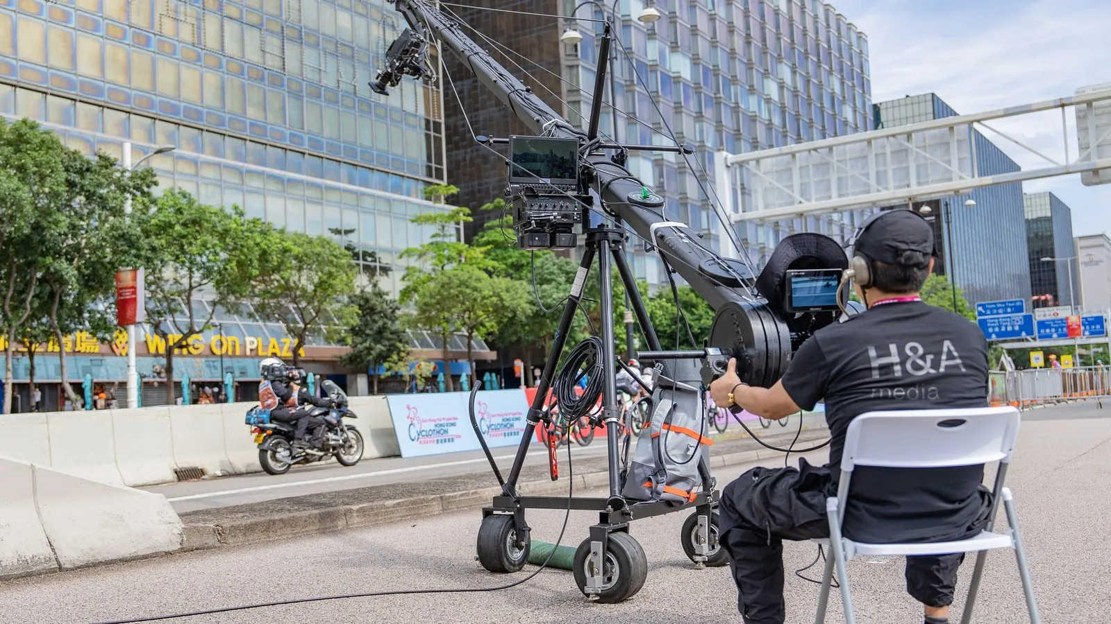 An H&A Media operator running a jib camera on a closed street, Hong Kong towers rising behind
