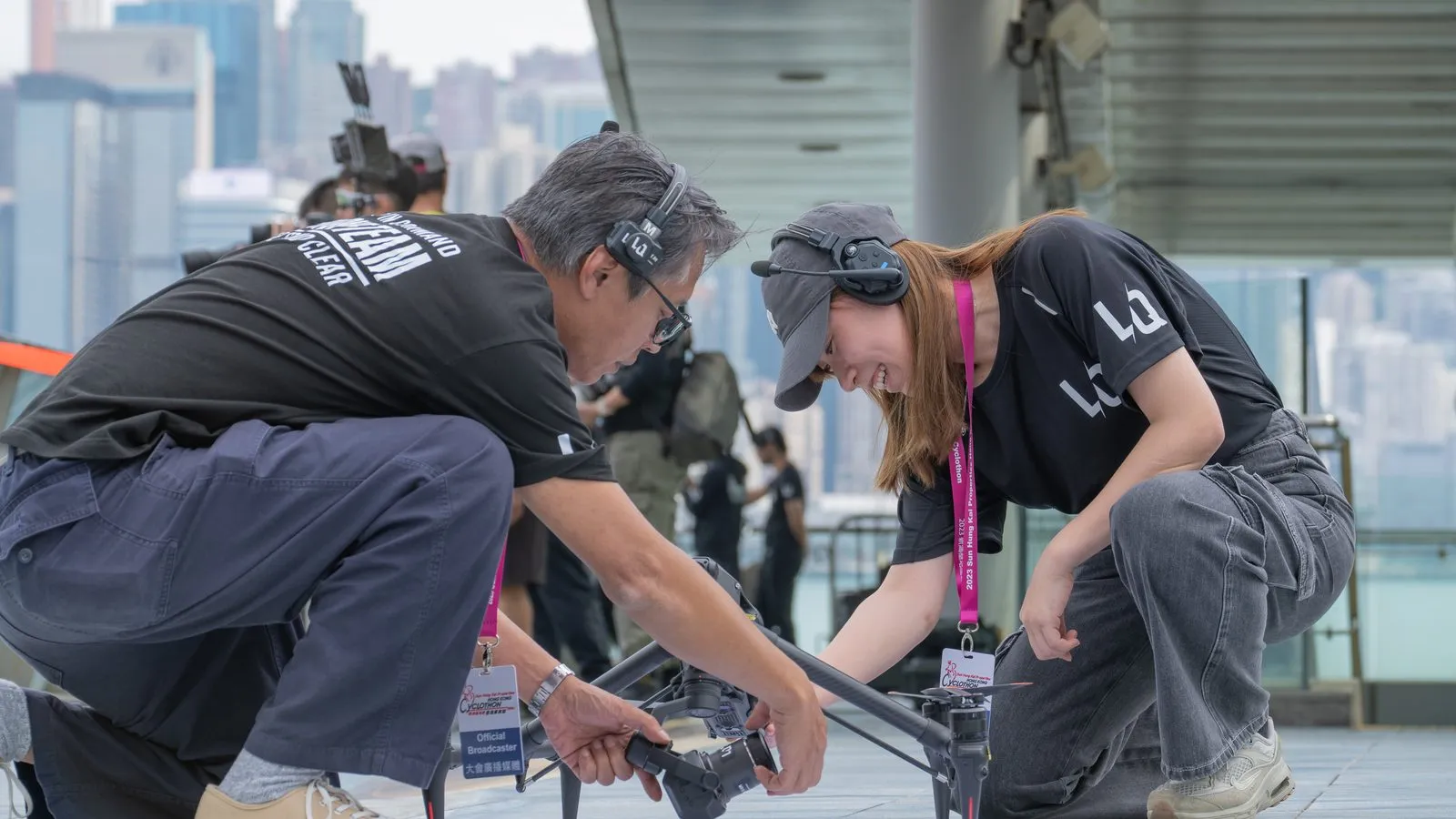 Two crew members preparing a drone for take-off on a rooftop above Victoria Harbour, Hong Kong