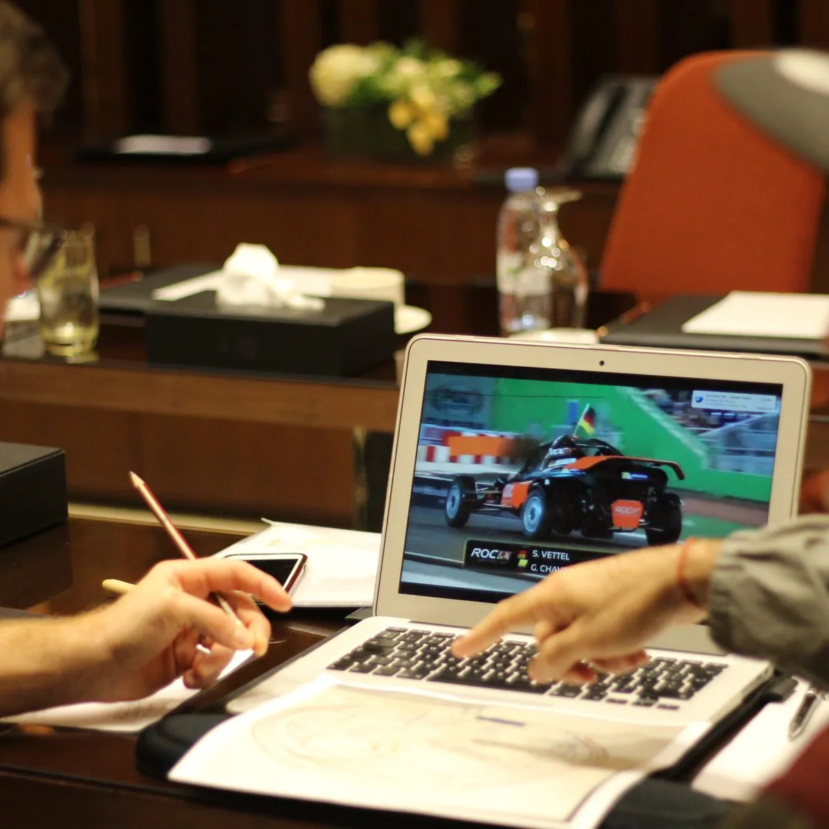 Two people reviewing race footage together on a laptop across a boardroom table
