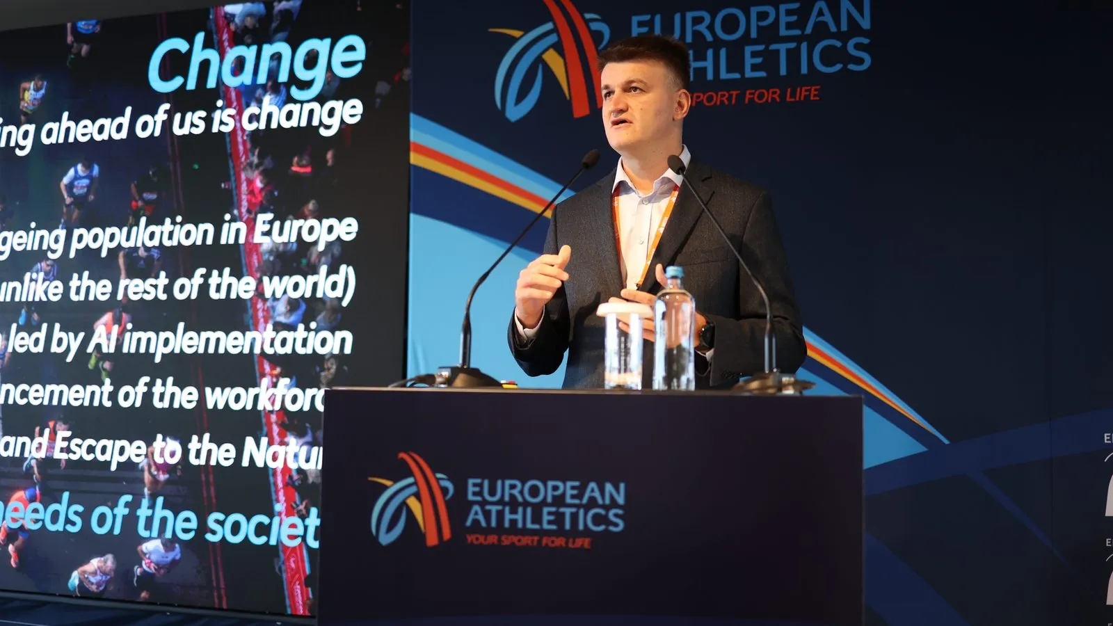 A speaker addressing the European Running Business Conference from the European Athletics podium, a slide headed “Change” behind him
