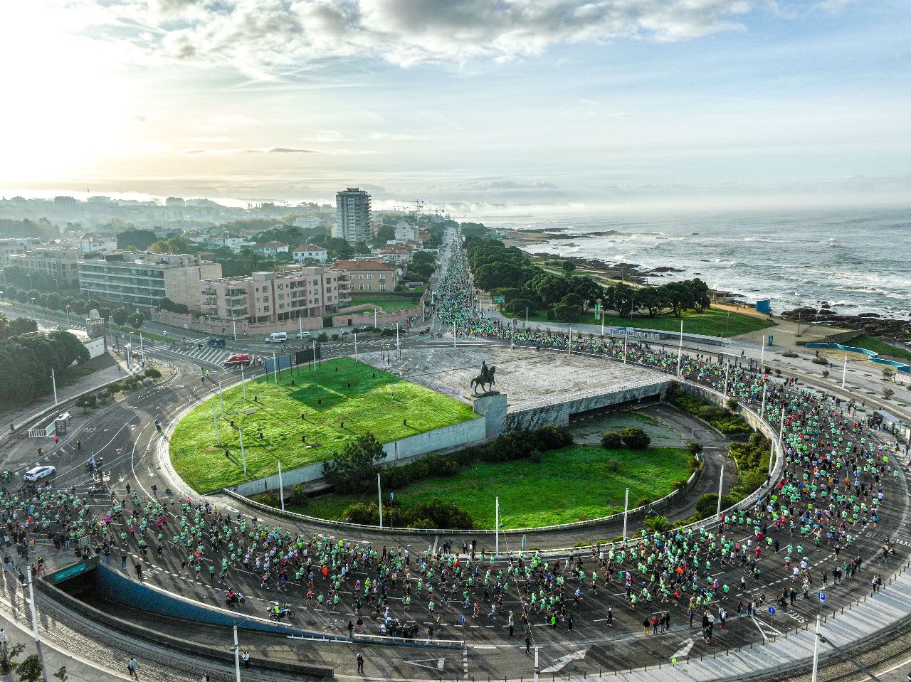 Runners rounding the coastal roundabout at first light during the EDP Porto Marathon, the Atlantic breaking alongside the course